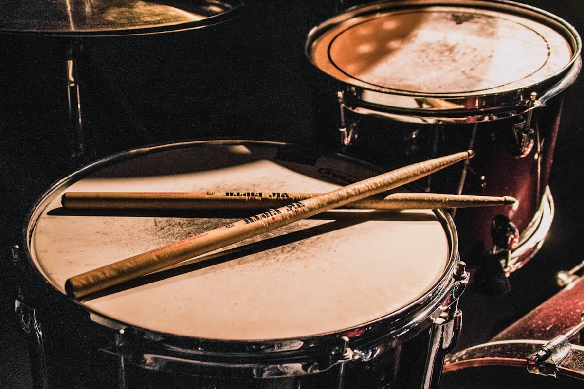 A drum with two wooden drumsticks resting on its head, lit warm against a dark background